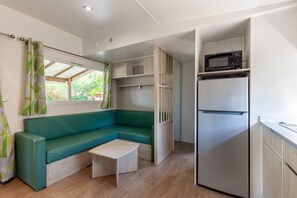 A compact kitchenette with a built-in microwave, a refrigerator, and a seating area with a bench and table. - Mobile Home 'Lou Soleil 80' with Shared Pool, Wi-Fi and Air Conditioning (Carry-le-Rouet)