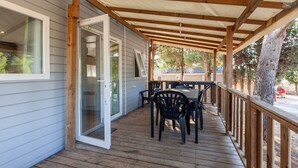 A covered outdoor deck with a table and chairs, wooden railings, and a sliding glass door leading to a room.