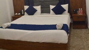 A hotel room with a wooden bed frame, a headboard with a grey and blue panel, white bedding, and a sign on the floor reading "HOLMES PLACE". - Hotel AU Villa (Etmadpur)