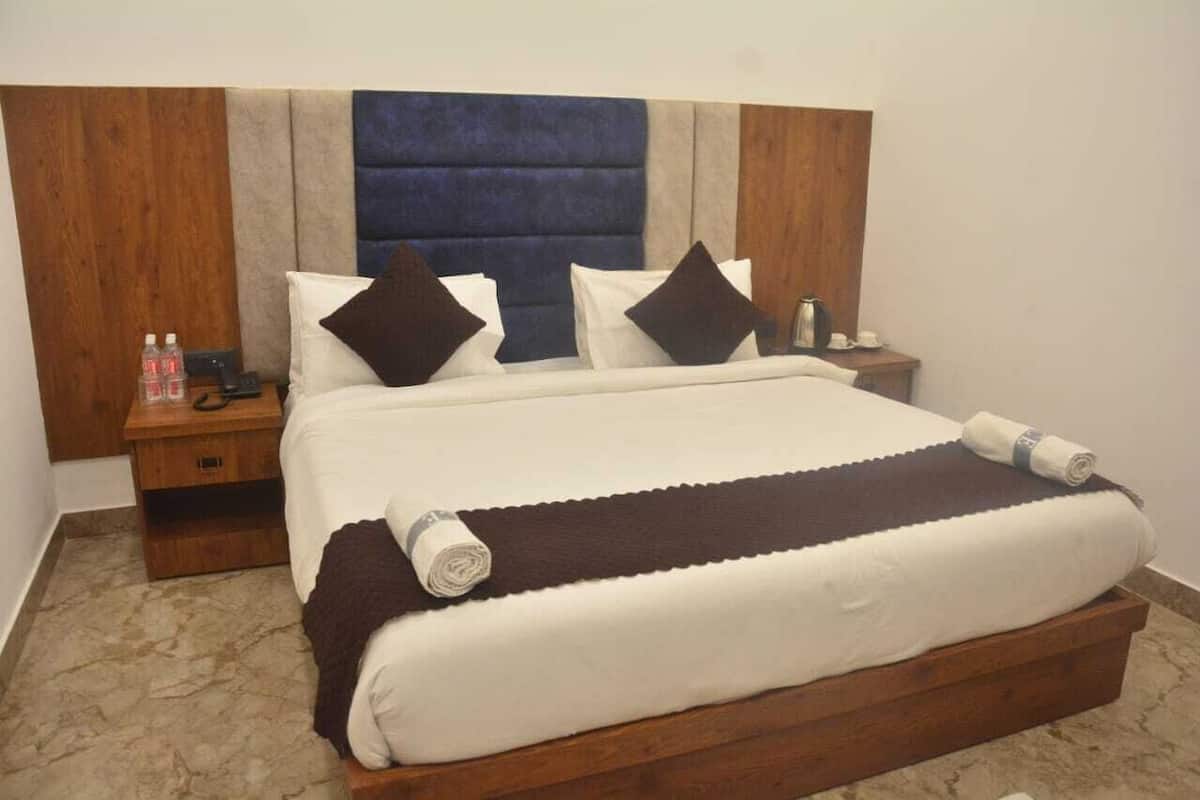 A neatly made bed with a dark headboard, white bedding, and two pillows. There is a wooden nightstand with a phone and a bottle of water beside the bed.