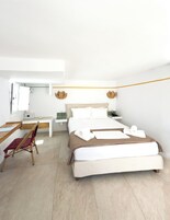 A modern hotel room with a bed, desk, chair, and a small table with a lamp.