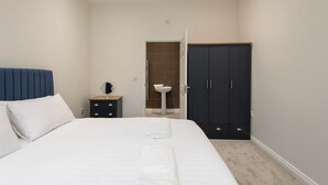 Een slaapkamer met een bed, een nachtkastje met spiegel, een garderobe en een badkamer met wastafel.