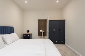 Un dormitorio con una cama, una mesita de noche con espejo, un armario y un baño con lavamanos.