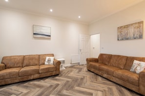Ein Wohnzimmer mit zwei braunen Sofas, einem weißen Heizkörper und einer Tür im Hintergrund.