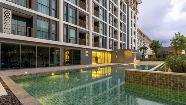 Een modern hotel met een zwembad, meerdere balkons en een fitnessruimte, zichtbaar door de glazen deuren.