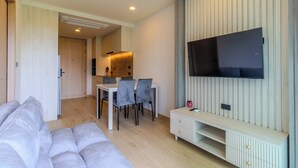 Een moderne woonkamer met een bank, eettafel, stoelen, een aan de muur bevestigde televisie en een keuken op de achtergrond.