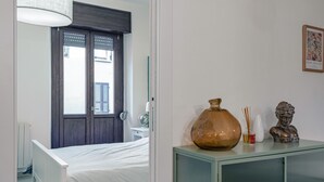 Quarto com uma cama, penteadeira, um vaso e um busto sobre a penteadeira.
