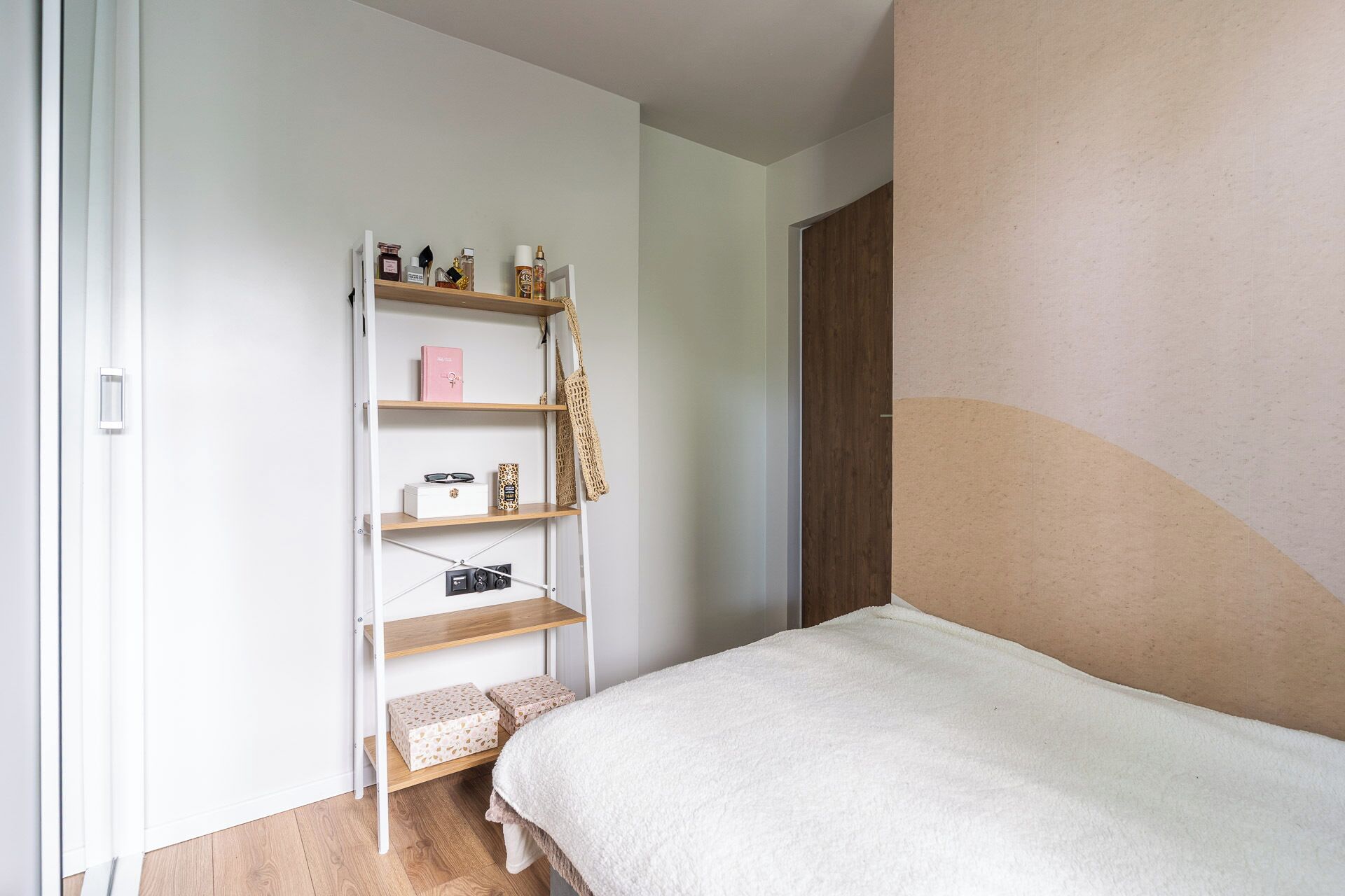 A bedroom with a bed, a wooden shelf unit, and a wardrobe.