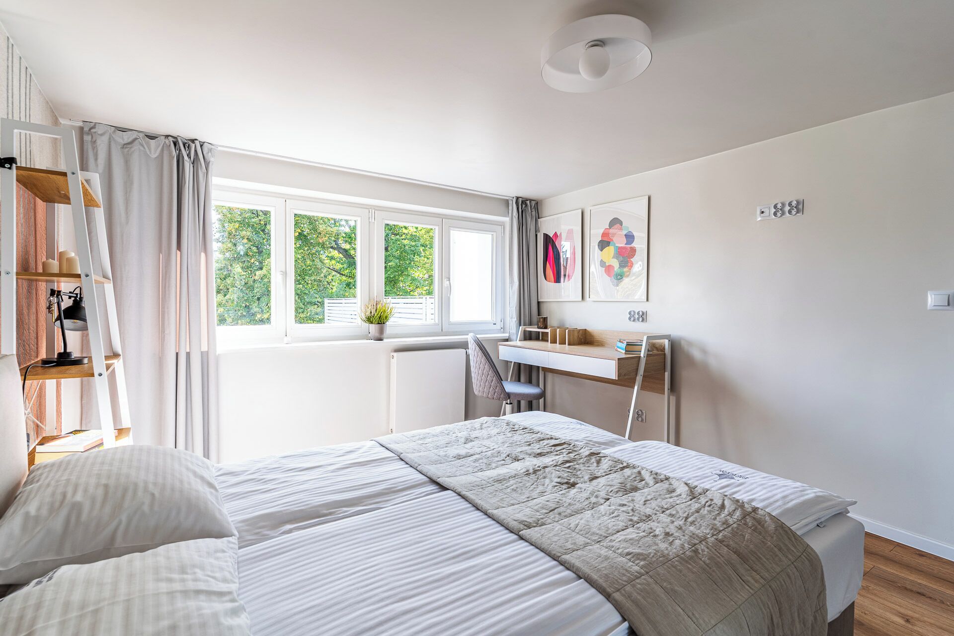 A bedroom with a bed, a desk, a chair, a radiator, and a window with curtains.