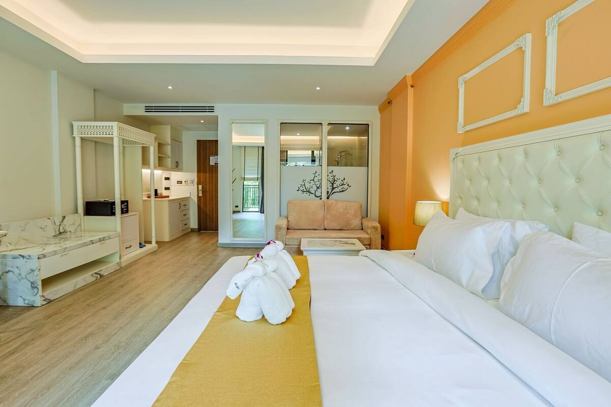 Een hotelkamer met een bed, een bank, een bureau en een badkamer zichtbaar door een glazen deur.