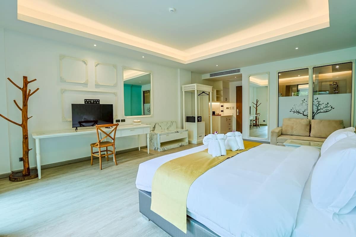Een hotelkamer met een groot bed, een bureau met een televisie, een stoel, een bank en een spiegel.