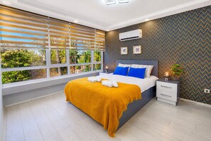 Un dormitorio moderno con una cama grande, una mesita de noche, una ventana con persianas y un aire acondicionado de pared.
