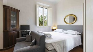 Een slaapkamer met een bed, een stoel, een kast, een televisie en een raam.