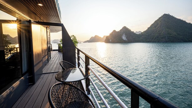 A deck with outdoor seating overlooking a body of water and a mountainous landscape. - Dragon Premium Cruise (Tuan Chau)