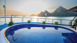 A swimming pool with a view of a mountainous coastline at sunset. - Dragon Premium Cruise (Tuan Chau)