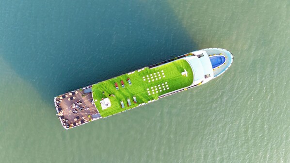 An aerial view of a cruise ship with a grassy deck, outdoor seating, and a swimming pool.