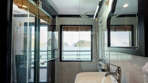A modern bathroom with a large bathtub, a glass-enclosed shower, and a view of the sea through a large window. - Dragon Premium Cruise (Tuan Chau)
