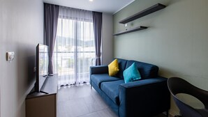 Un soggiorno moderno con un divano blu, una TV su un mobile in legno e un'ampia finestra con tende leggere.