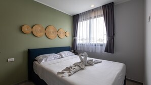 Un letto rifatto con lenzuola bianche e un'accogliente disposizione di asciugamani a forma di cuore, una testiera blu e una parete decorata con opere d'arte tessute a cerchio.
