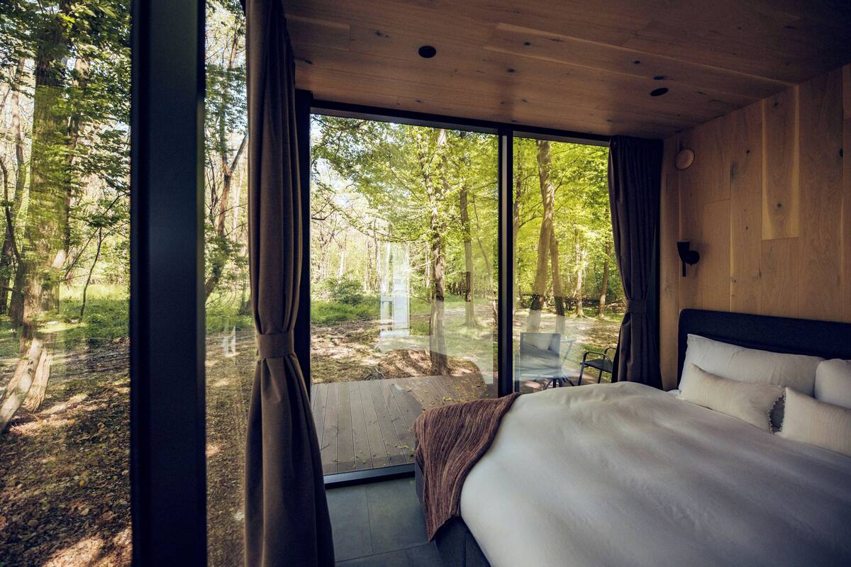 A bedroom with a large window, a bed, and a view of a forest.