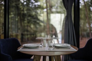 Mesa lista para comer con platos, vasos y una jarra de leche, con vista a un bosque por la ventana.