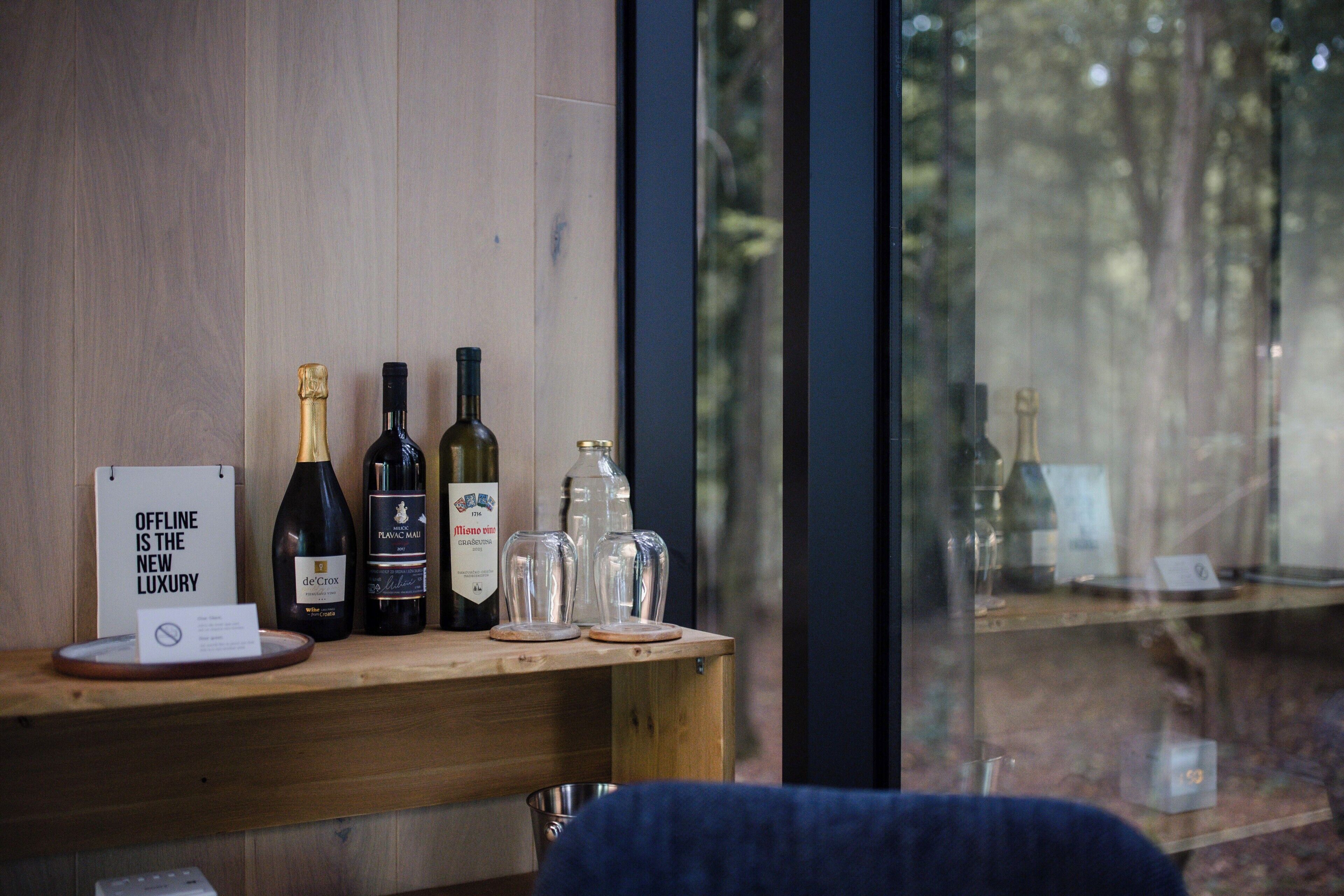 A wooden counter with wine bottles, glasses, and a sign.