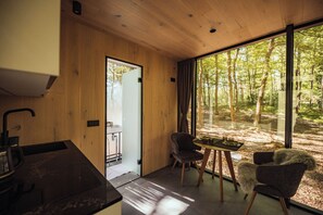 A modern interior with wooden walls, a dining area with chairs, a table, and a view of a forest through large windows. - Mala Vila (Gradec)