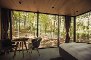 Un dormitorio con un ventanal grande, una cama, una silla y una mesita.