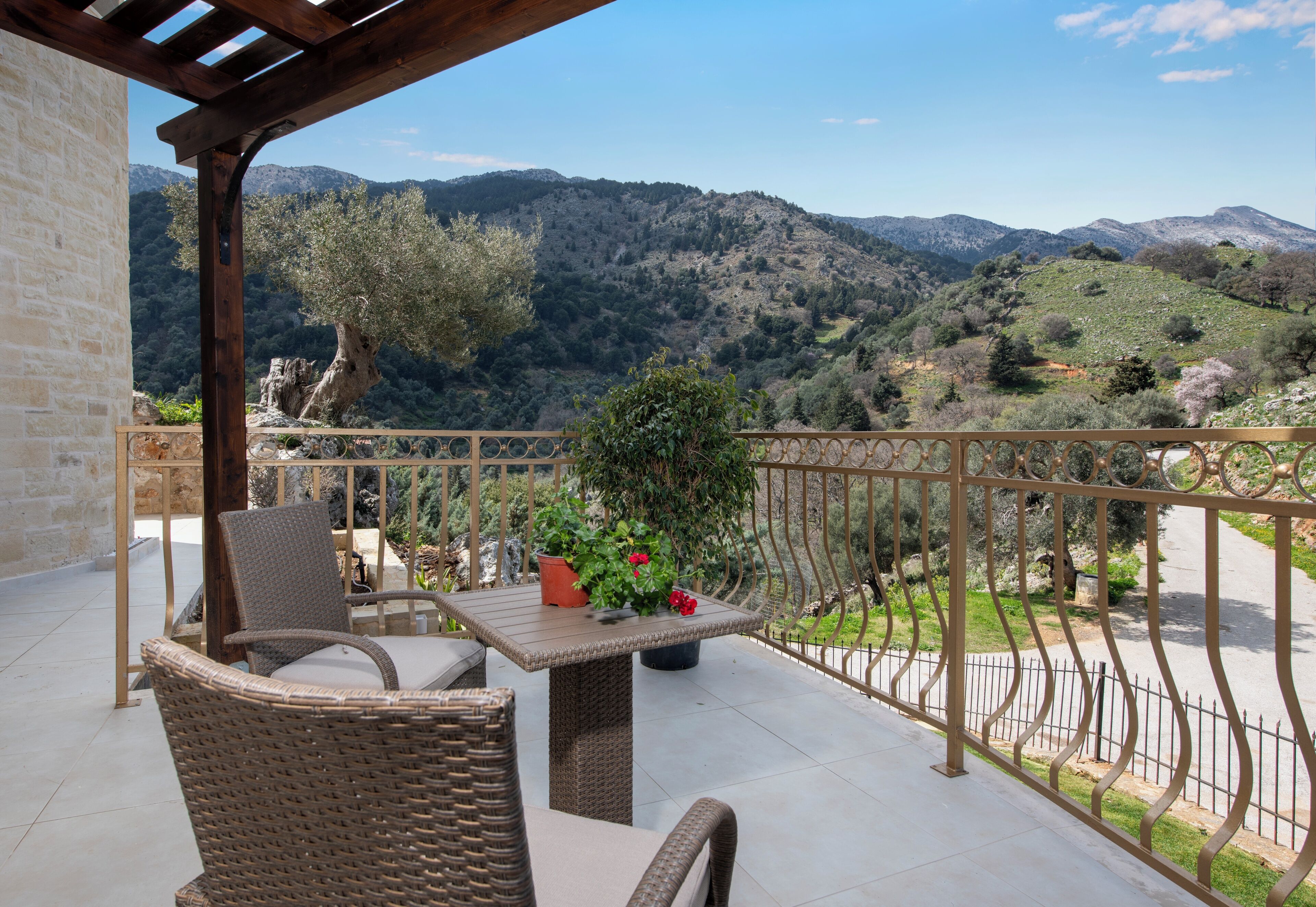 A balcony with wicker furniture, a table with a potted plant, and a view of a mountainous landscape.