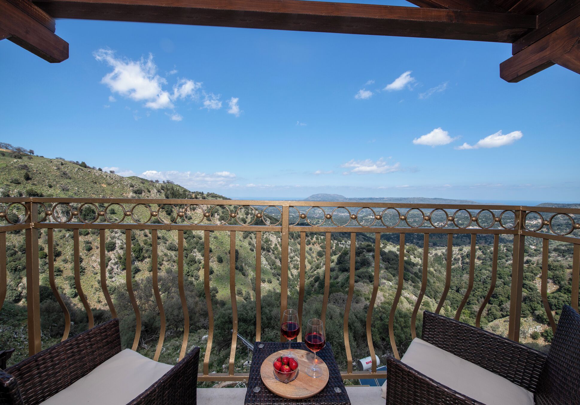 A balcony with wicker furniture and a table with a bowl of fruit and glasses of red wine.