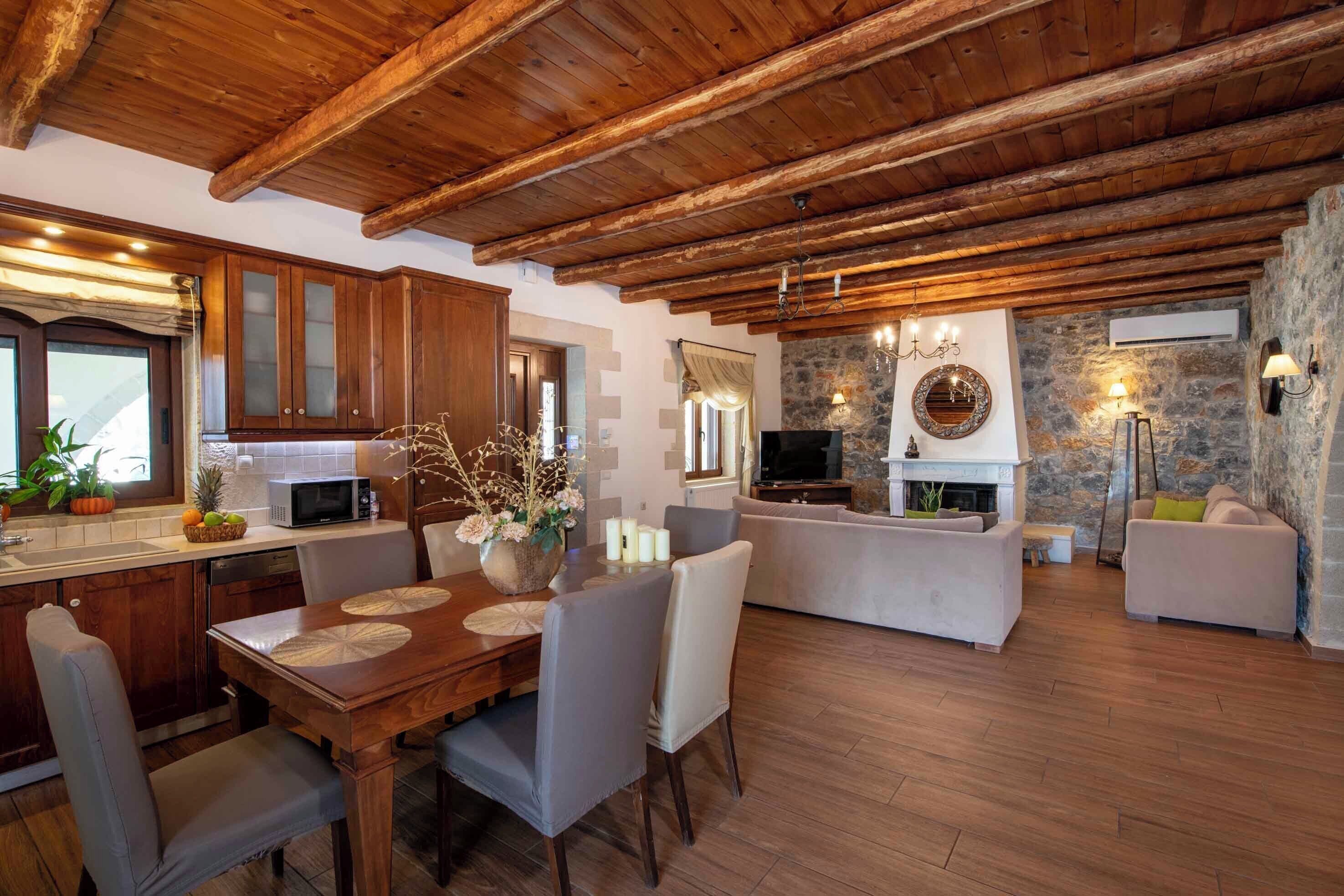 Un salón espacioso con techo de madera, chimenea de piedra y una cocina moderna con armarios de madera.