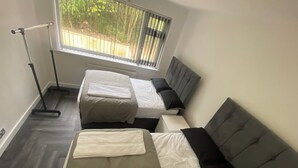 A room with two beds, a window with blinds, a radiator, and a treadmill.