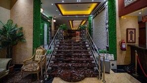 A grand staircase with marble steps leading to a higher floor, flanked by green wall panels and a fire extinguisher on the right. - Misk Umm Al Qura Hotel (Makkah)