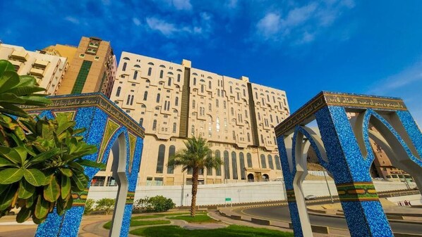 A large building with a central courtyard, surrounded by palm trees and a clear blue sky.