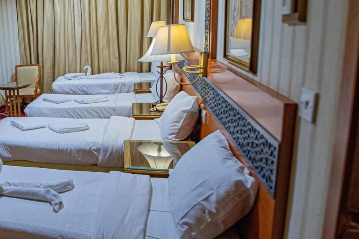 Habitación de hotel con tres camas, cada una con ropa de cama y toallas blancas, una lámpara de noche y un espejo.