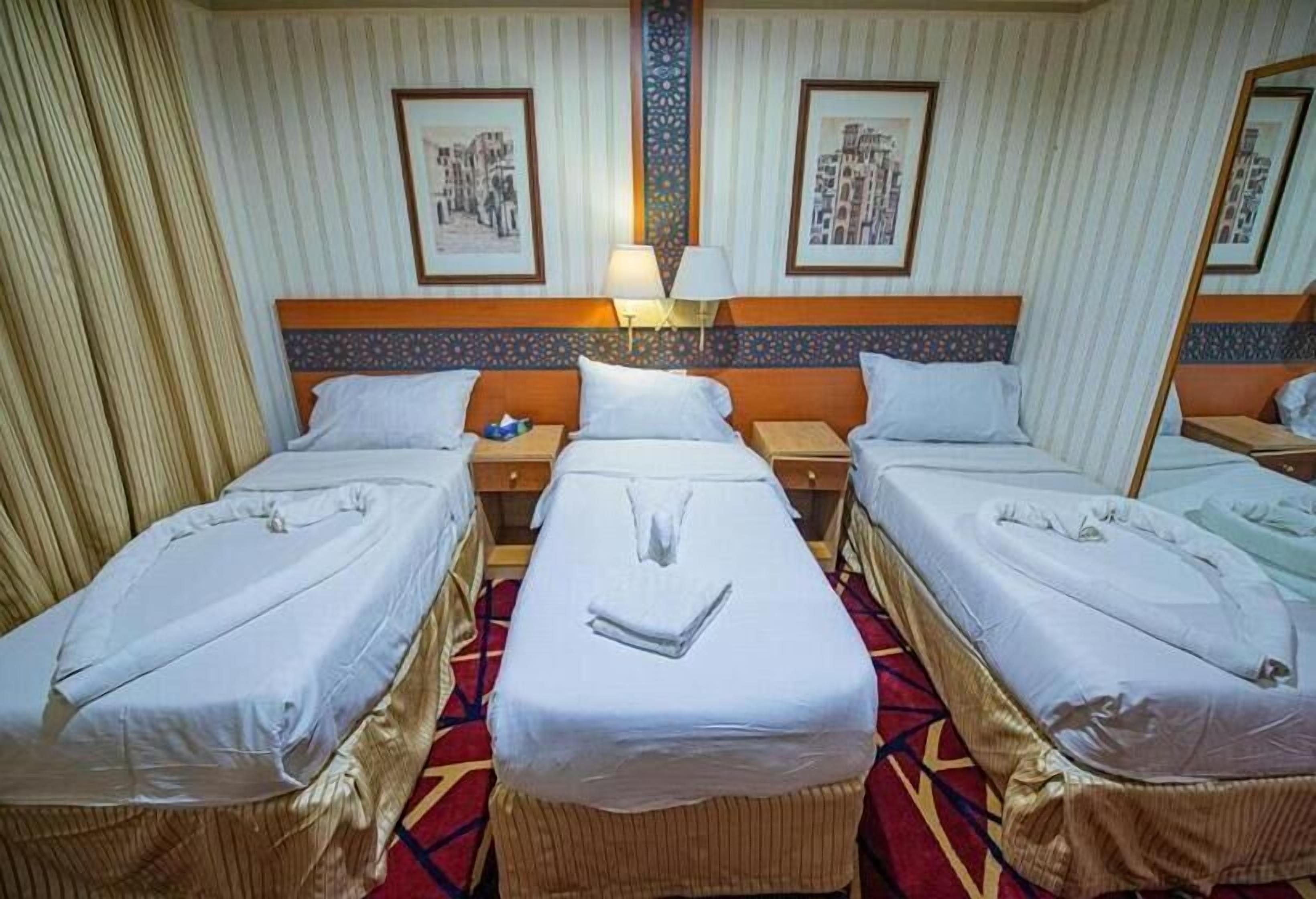 A hotel room with two single beds, a nightstand with a lamp, and a large mirror.