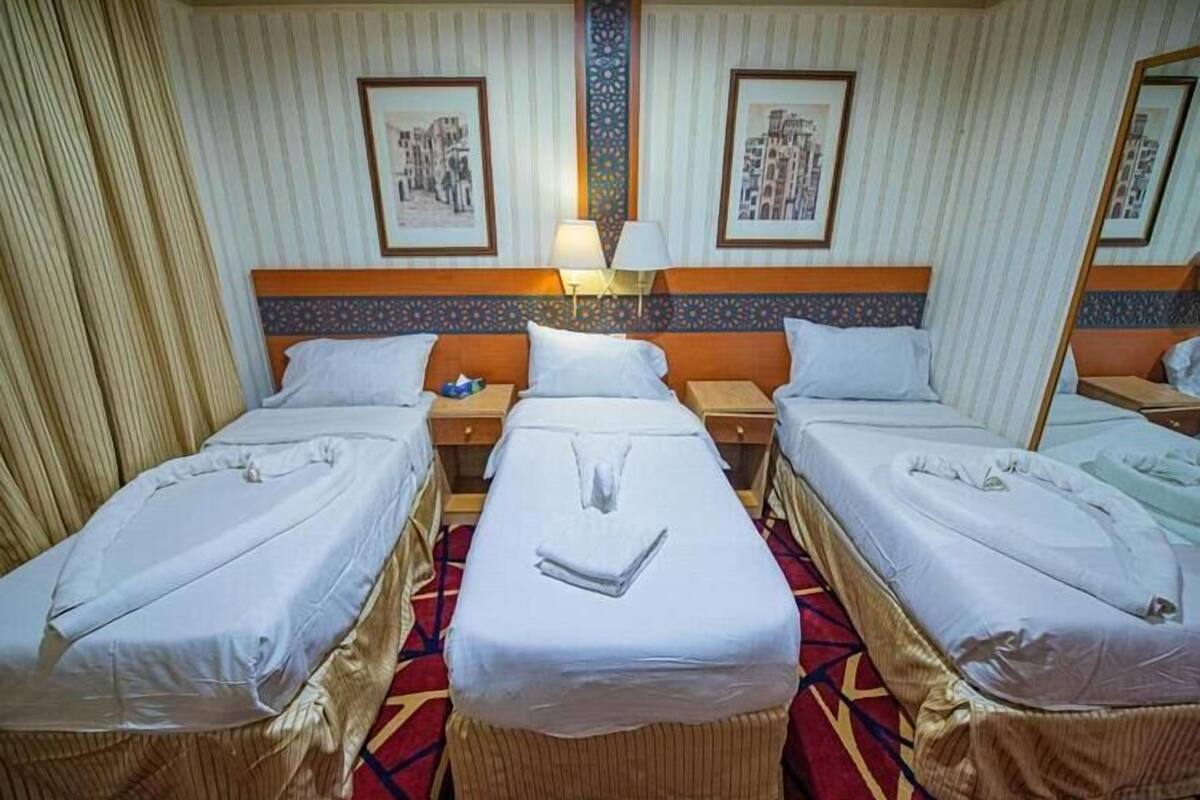 Una habitación de hotel con dos camas individuales, una mesita de noche con lámpara y un espejo grande.