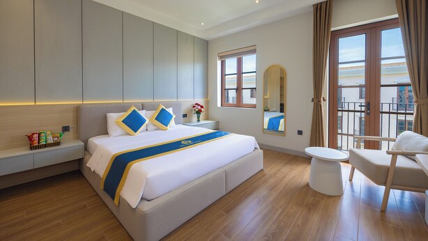 Una habitación de hotel moderna con una cama grande, una mesita de noche, una silla y vistas al balcón.