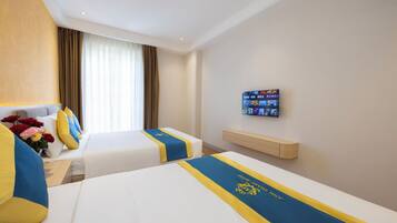 Habitación de hotel con dos camas, cada una con cubrecama azul y amarillo, cabecero de madera, mesita de noche con un florero y televisor montado, además de un estante de madera.