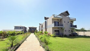 A modern multi-story building with a central courtyard, surrounded by well-maintained gardens and a paved walkway. - Gold Lion Resort (Talala)