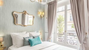 Une chambre d’hôtel avec un grand lit, un miroir, un lustre et une vue sur le balcon extérieur.