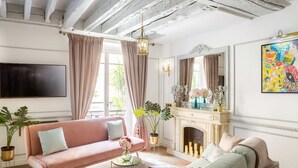 Un salon avec un canapé rose, un canapé vert, une cheminée et un téléviseur fixé au mur.