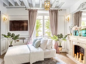 A bedroom with a bed, a fireplace, and a large window with curtains. - Merveil Luxury Suite - Louvre Rambuteau (Paris)