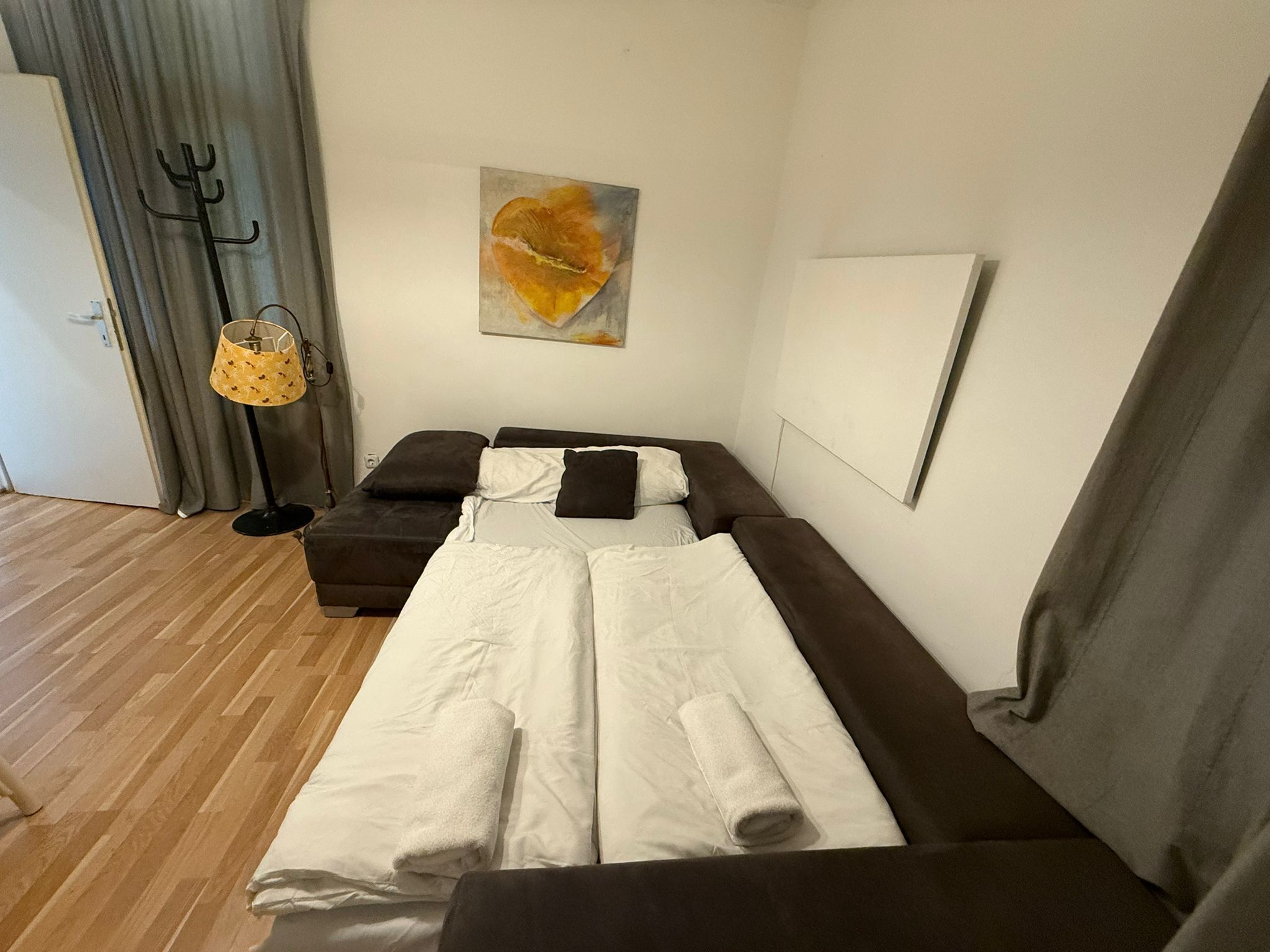 Ein Schlafzimmer mit einem Bett, einem Schlafsofa, einem Kleiderhaken und einem Bild an der Wand.