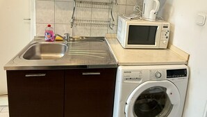 Uma cozinha compacta com armários marrom-escuro, uma pia de aço inoxidável, um micro-ondas e uma máquina de lavar de abertura frontal.