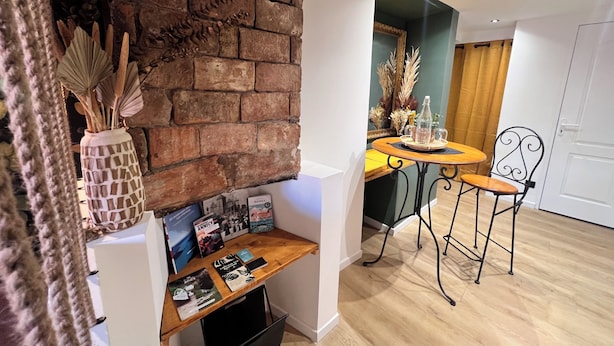 A modern kitchen with a brick wall, wooden countertop, and a dining area with a chair and table.