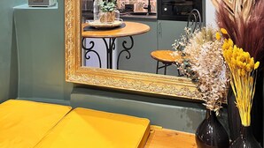 A room with a large ornate mirror, a small round table with a vase of dried flowers, and a yellow bench.