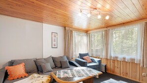 A cozy room with a wooden ceiling, a sofa with cushions, a chair, a small table, and large windows with curtains. - Bungalow '7 - Finnhütte' with Private Terrace and Shared Garden (Niesky)