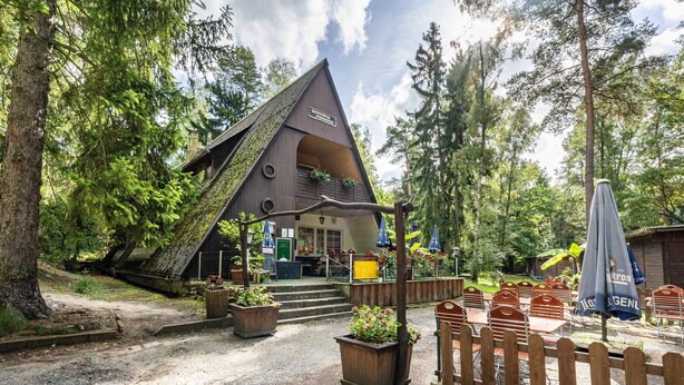 A rustic cabin with a sloped roof, wooden deck, and outdoor seating area. - Bungalow '7 - Finnhütte' with Private Terrace and Shared Garden (Niesky)