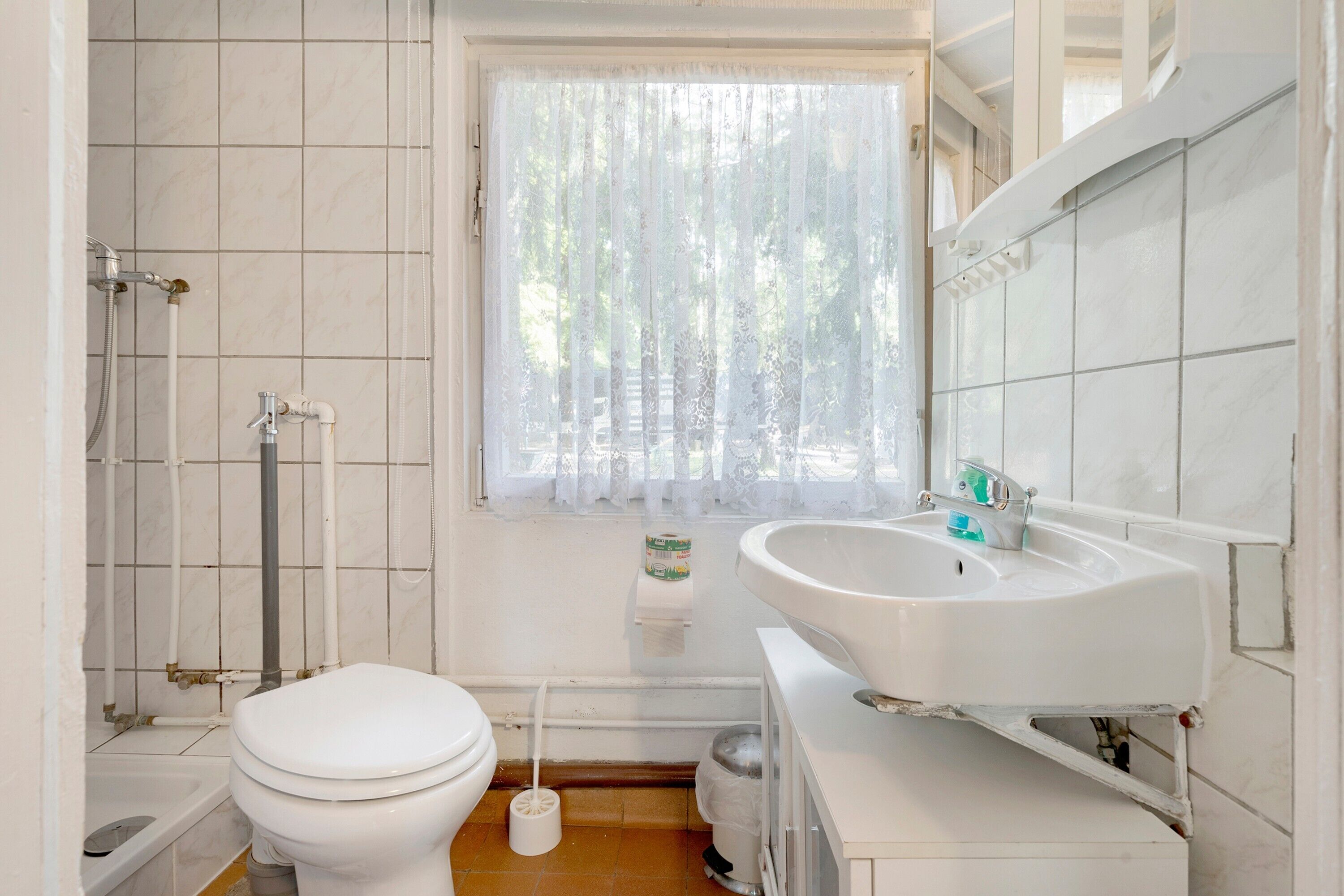 A bathroom with a toilet, sink, shower, and window with curtains.
